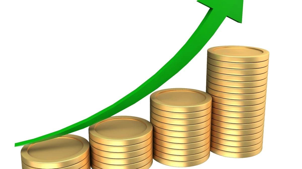 Stacks of gold coins rising under an upward-trending green arrow