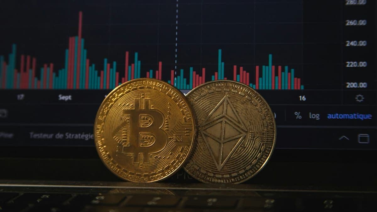 Physical Bitcoin and Ethereum coins in front of a red and green crypto price chart