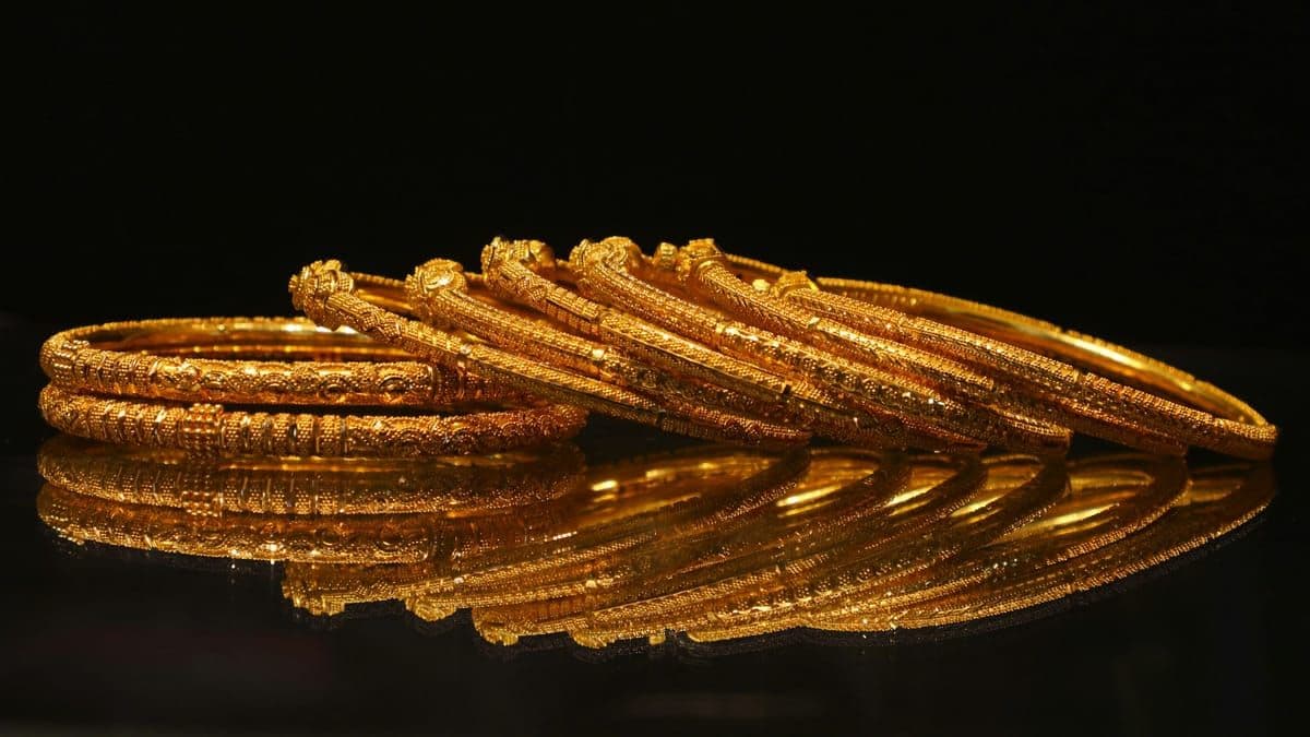 A stack of ornate gold bangles on a reflective surface