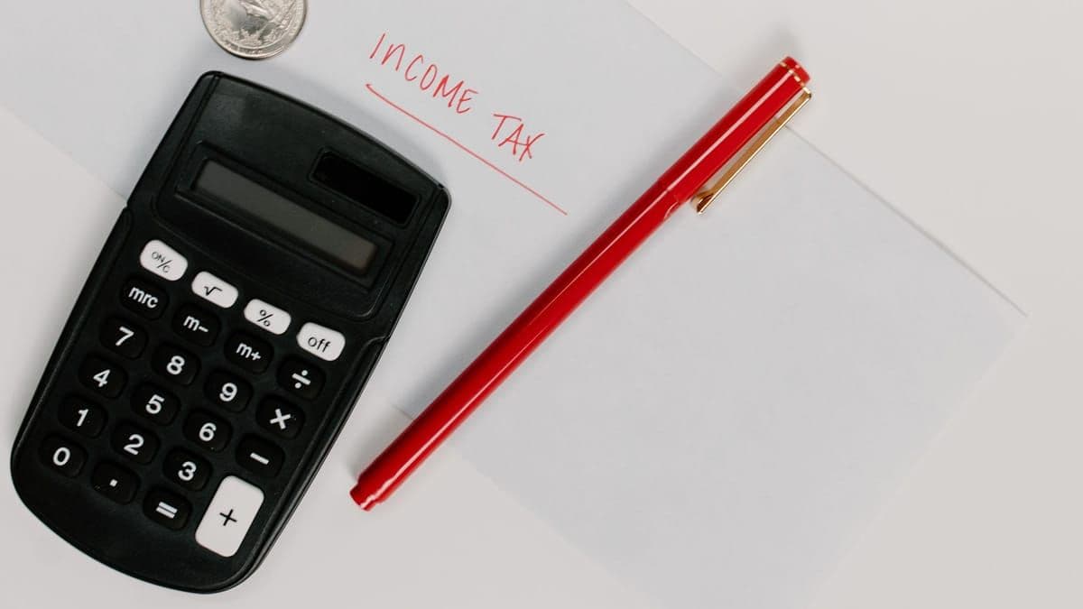 A black calculator beside a pen and a few coins on a desk